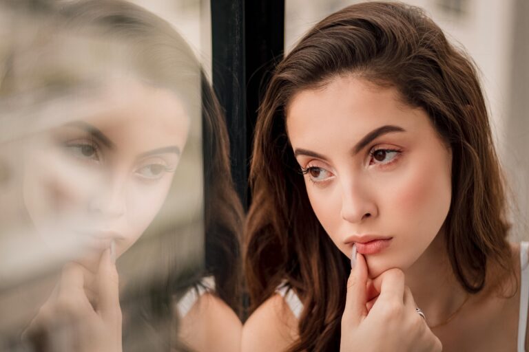 A woman staring thoughtfully through a glass. The glass shows her reflection.