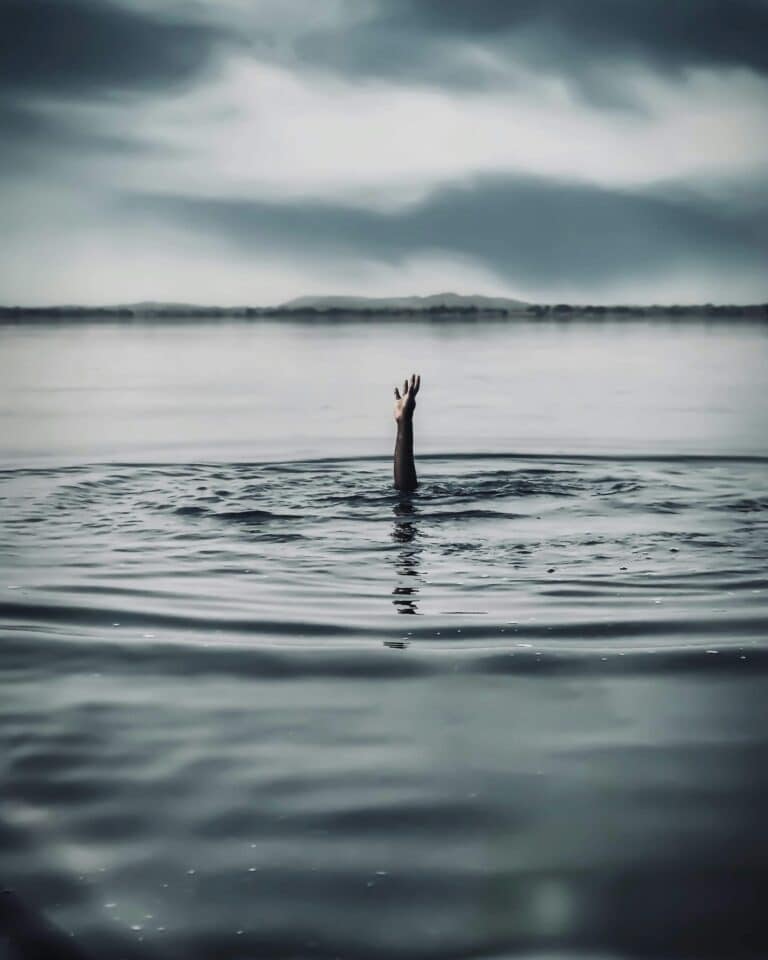 Hand reaching out of dark water under cloudy sky, symbolizing struggle in mental health care for neurodivergent people